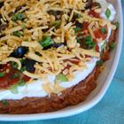 Seven Layer Taco Dip with refried beans, cream cheese, and salsa in a serving dish